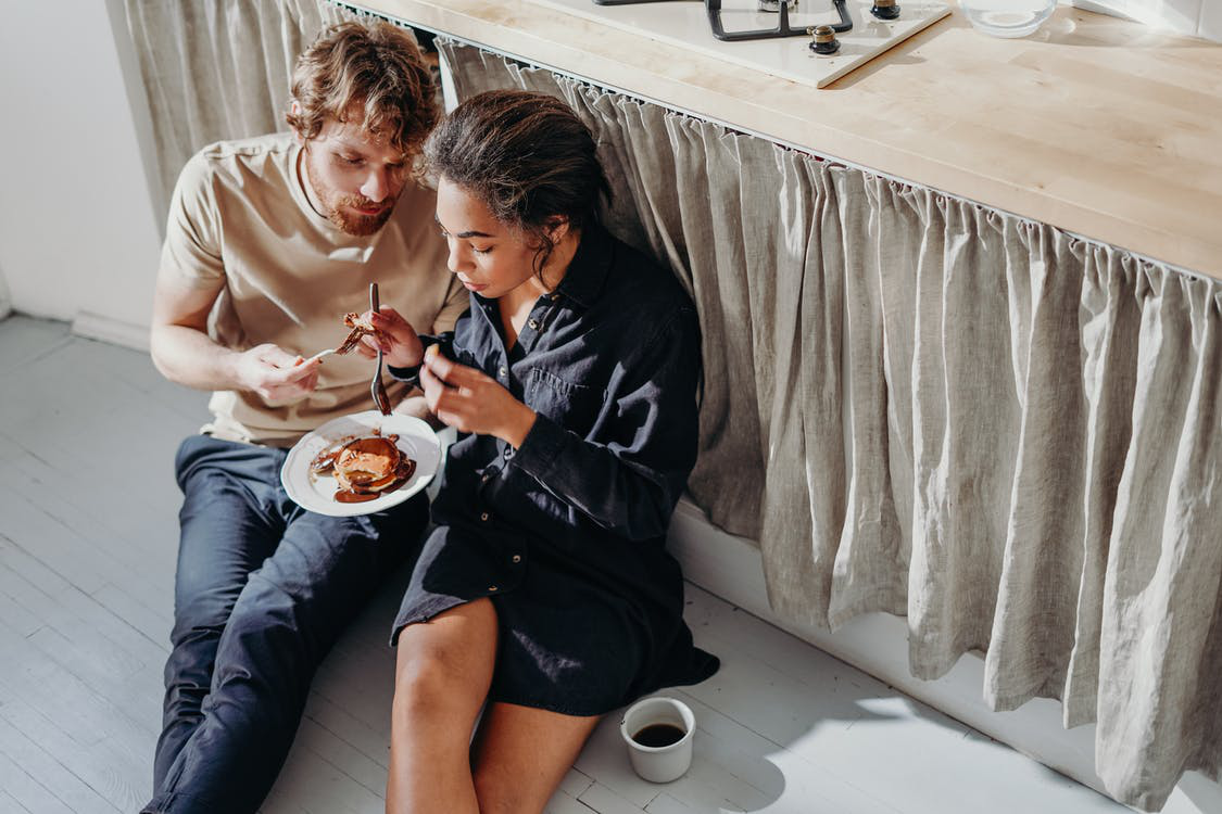 A man and woman sitting on the floor and eating some food together