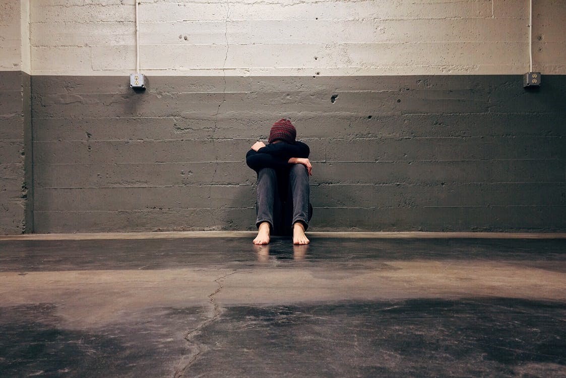 A man sitting on the floor with his head in on his arms feeling sad after an angry outburst