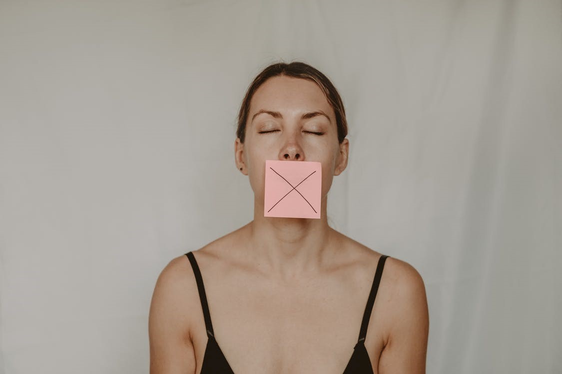 A woman with a sticky note on her face with an X on it to depict how domestic violence victims are often forced into silence