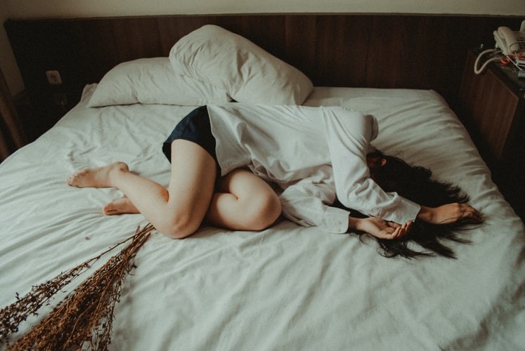 A woman curls up in bed, crying in pain and grief