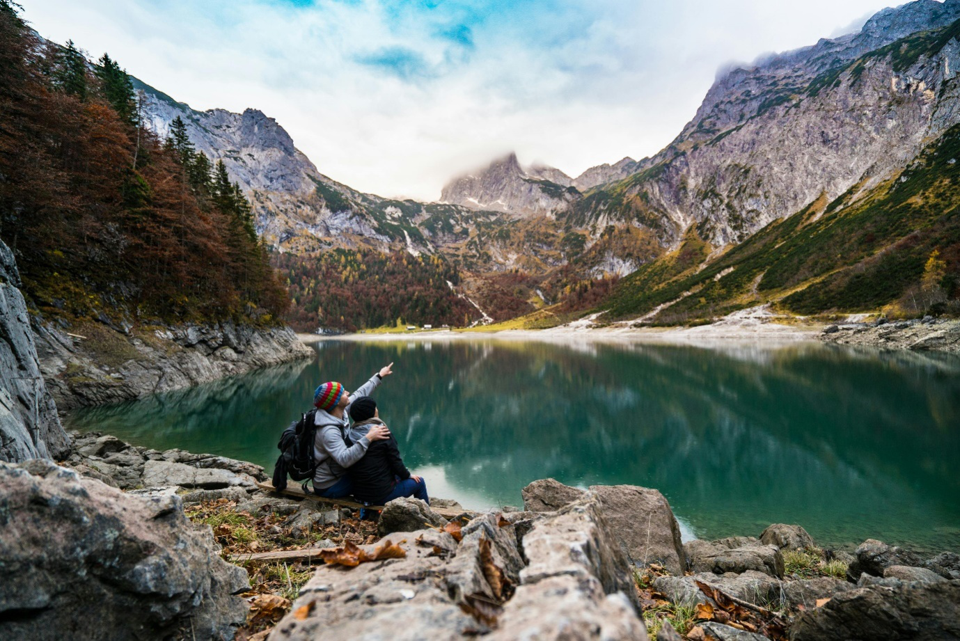 a couple sitting on a rock beside a lake