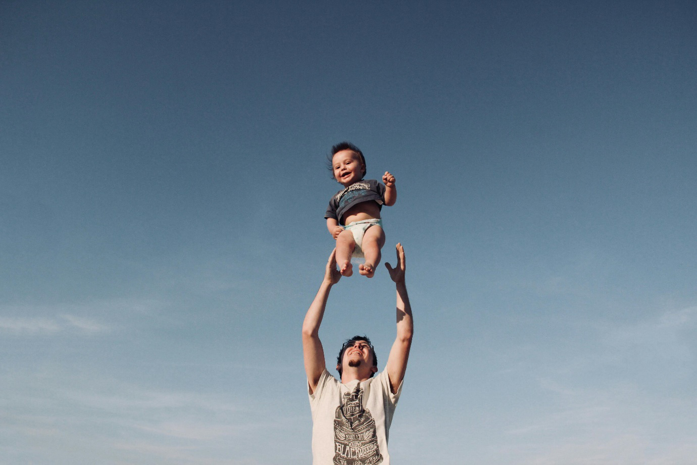 a man raising baby under blue sky