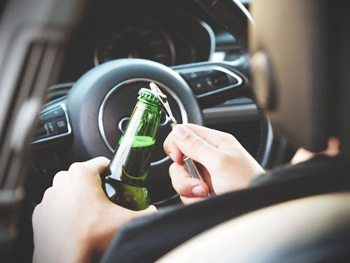 Person drinking alcohol behind the wheel, illustrating the risks of alcohol dependency and the importance of seeking treatment.