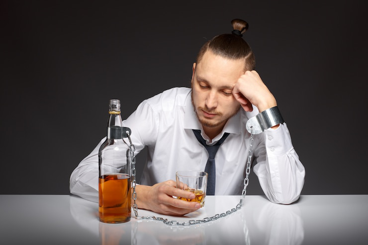 Person sitting with head down and holding a bottle of alcohol, reflecting emotional distress linked to substance use.